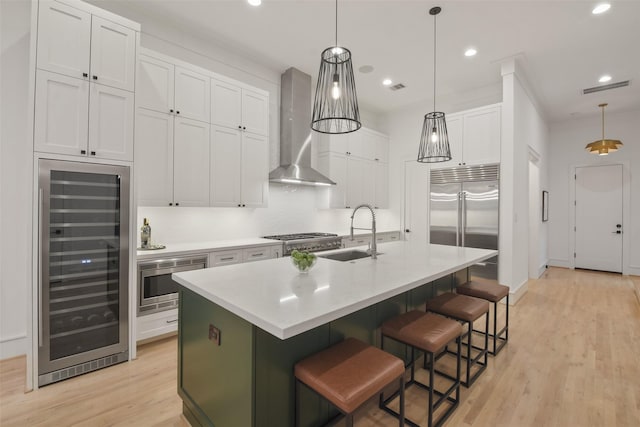 kitchen featuring sink, wall chimney exhaust hood, wine cooler, an island with sink, and white cabinets