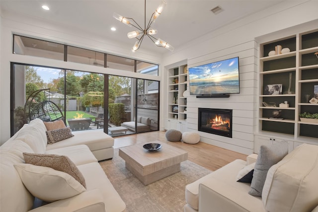 living room featuring built in shelves, a fireplace, a notable chandelier, and light hardwood / wood-style flooring