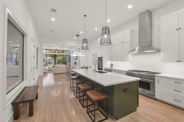 kitchen with a center island with sink, white cabinets, wall chimney range hood, sink, and high end stainless steel range