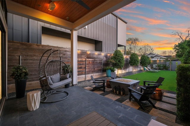 deck at dusk with a fire pit, ceiling fan, a patio area, and a lawn