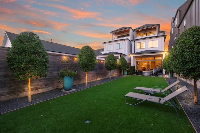 back house at dusk featuring a patio and a lawn