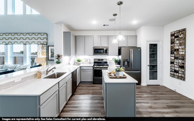 kitchen with kitchen peninsula, appliances with stainless steel finishes, gray cabinetry, sink, and decorative light fixtures