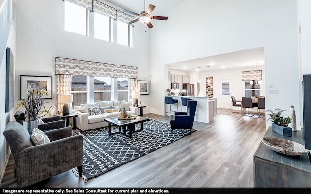 living room featuring ceiling fan with notable chandelier, wood-type flooring, and a towering ceiling