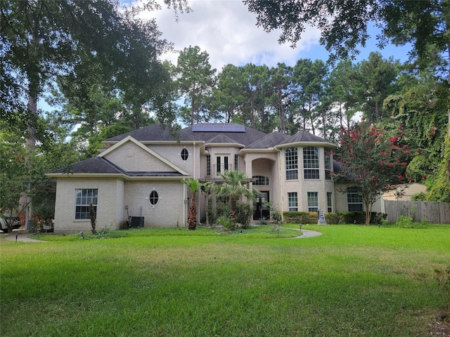 view of front facade featuring solar panels, central AC unit, and a front lawn