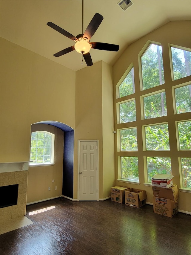 unfurnished living room with a tiled fireplace, a wealth of natural light, ceiling fan, and dark wood-type flooring