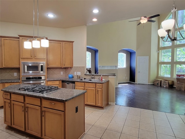 kitchen with kitchen peninsula, stainless steel appliances, sink, light tile patterned floors, and a center island