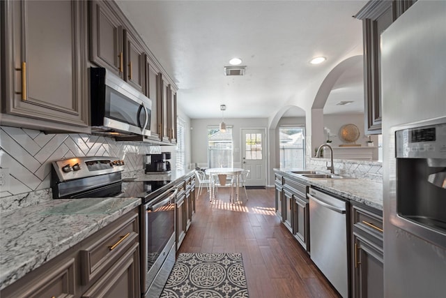 kitchen featuring stainless steel appliances, light stone counters, decorative backsplash, sink, and decorative light fixtures