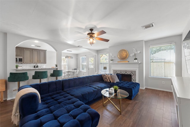 living room with a tile fireplace, dark wood-type flooring, and ceiling fan