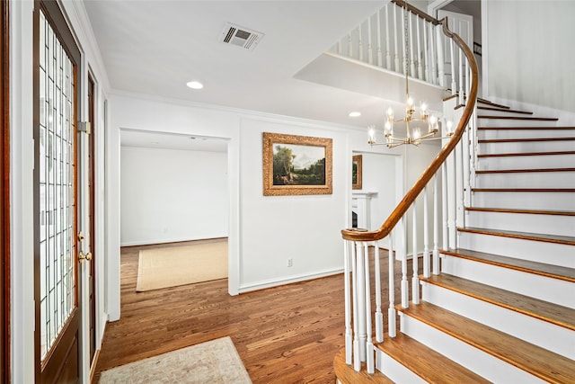 foyer with wood-type flooring, a healthy amount of sunlight, crown molding, and a notable chandelier