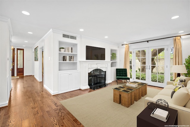 living room featuring french doors, light wood-type flooring, built in shelves, and crown molding