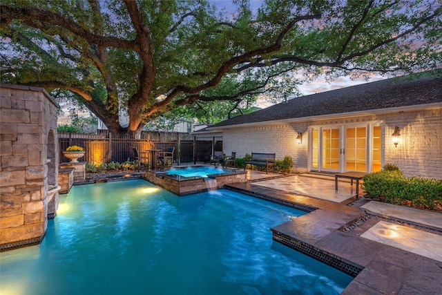 pool at dusk with a patio area, an in ground hot tub, and pool water feature