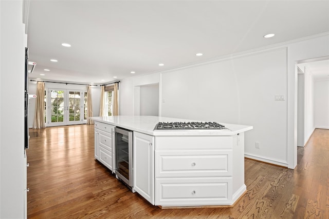 kitchen with white cabinets, beverage cooler, ornamental molding, a kitchen island, and stainless steel gas cooktop