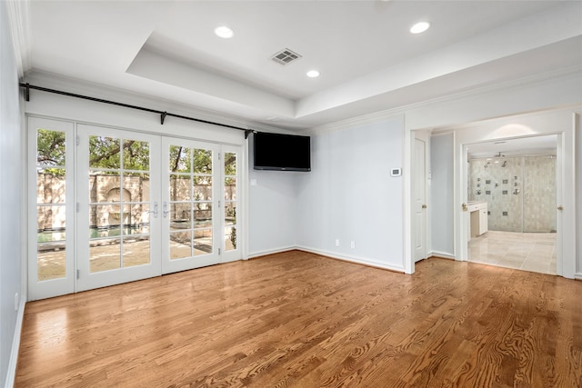 interior space with french doors, light wood-type flooring, a raised ceiling, and crown molding