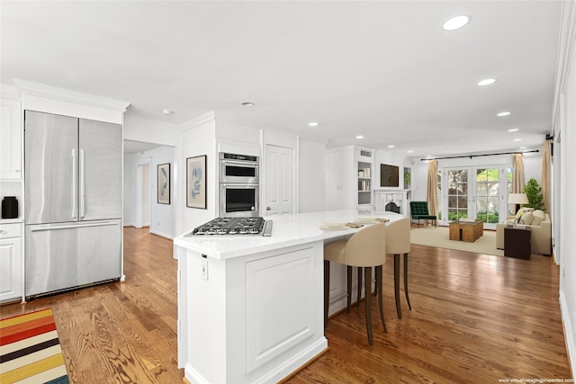 kitchen with white cabinetry, light wood-type flooring, a kitchen bar, appliances with stainless steel finishes, and ornamental molding