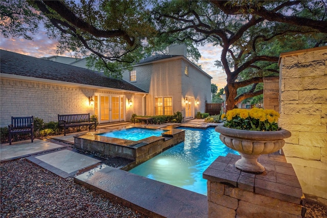 pool at dusk featuring a patio area and an in ground hot tub