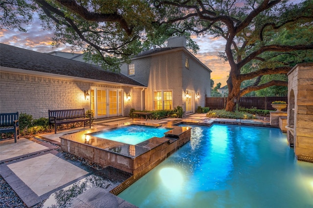 pool at dusk featuring an in ground hot tub