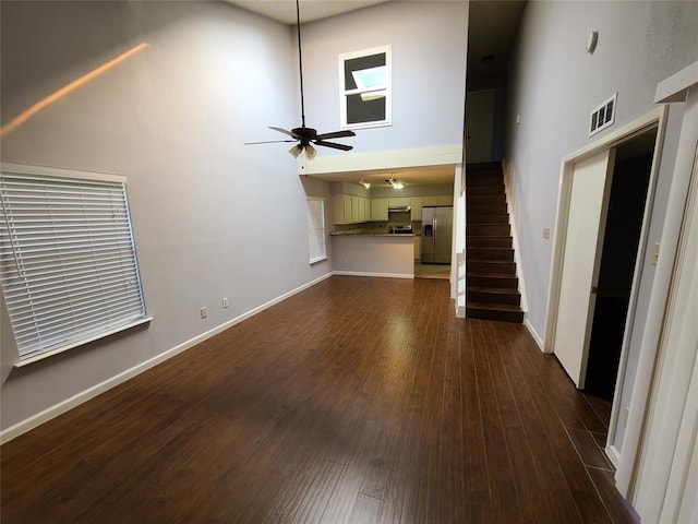 unfurnished living room with dark hardwood / wood-style flooring, a towering ceiling, and ceiling fan