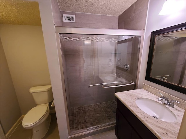 bathroom featuring vanity, toilet, a shower with shower door, and a textured ceiling