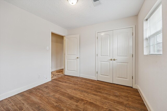 unfurnished bedroom with a textured ceiling, dark hardwood / wood-style flooring, and a closet