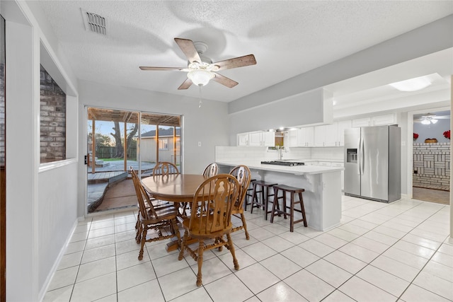 tiled dining space with a textured ceiling and ceiling fan