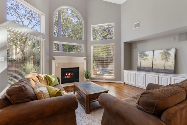 living room with plenty of natural light, light hardwood / wood-style floors, a towering ceiling, and a premium fireplace