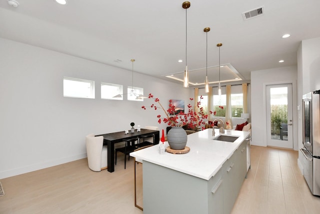 kitchen with stainless steel fridge, a kitchen island with sink, sink, gray cabinets, and light hardwood / wood-style floors