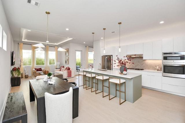 kitchen featuring pendant lighting, stainless steel appliances, a kitchen island with sink, and light hardwood / wood-style floors