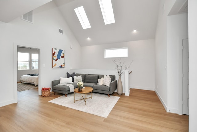 living room with plenty of natural light, a skylight, high vaulted ceiling, and light hardwood / wood-style flooring