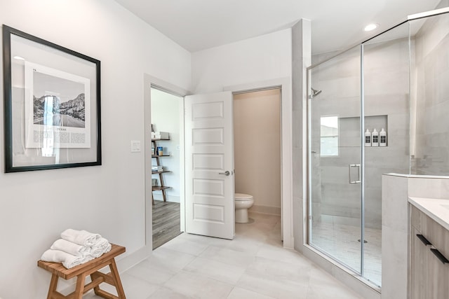 bathroom featuring a shower with door, vanity, and toilet