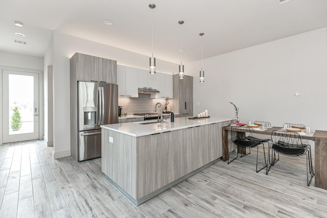 kitchen with backsplash, sink, stainless steel refrigerator with ice dispenser, light hardwood / wood-style flooring, and decorative light fixtures