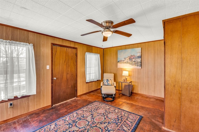 living area featuring crown molding, ceiling fan, a healthy amount of sunlight, and wood walls