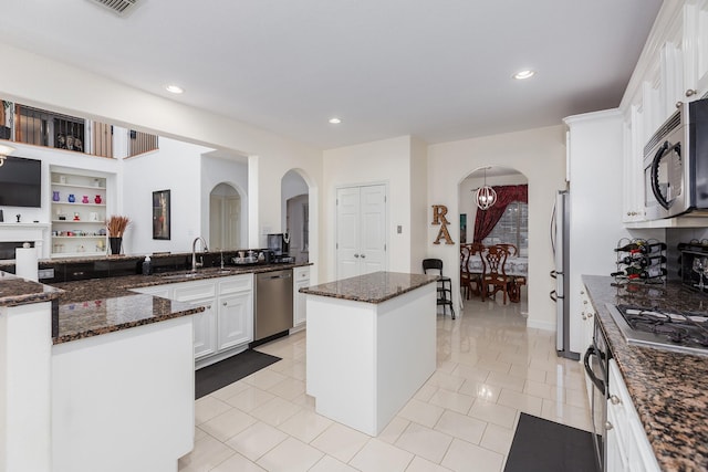 kitchen with dark stone countertops, a center island, white cabinets, and stainless steel appliances