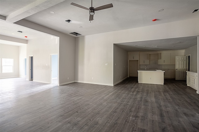 unfurnished living room with beamed ceiling, ceiling fan, and dark wood-type flooring