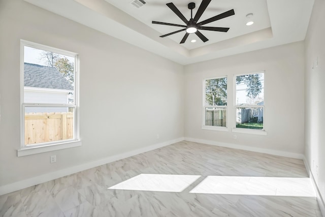 unfurnished room with a tray ceiling, a wealth of natural light, and ceiling fan