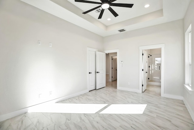 unfurnished bedroom with a raised ceiling, ensuite bath, and ceiling fan