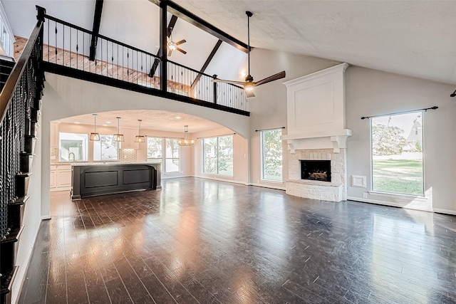 unfurnished living room featuring a stone fireplace, dark hardwood / wood-style flooring, and a towering ceiling