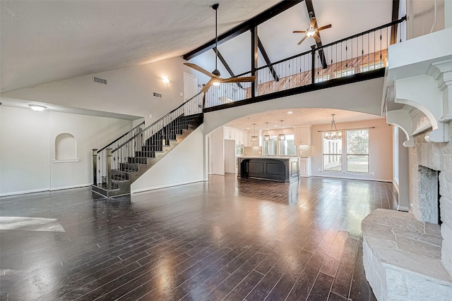 unfurnished living room with ceiling fan with notable chandelier, dark wood-type flooring, and high vaulted ceiling