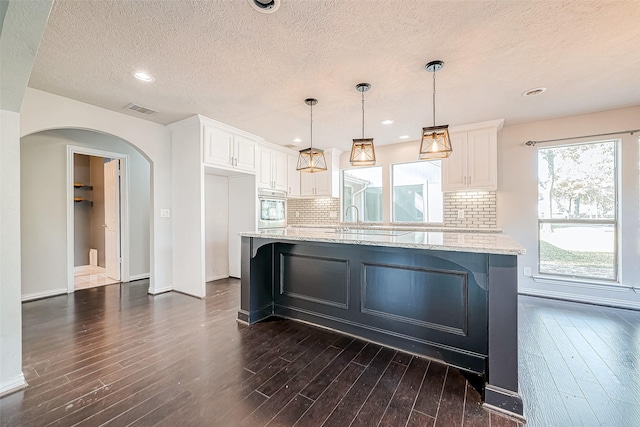 kitchen with light stone countertops, backsplash, stainless steel oven, pendant lighting, and white cabinetry