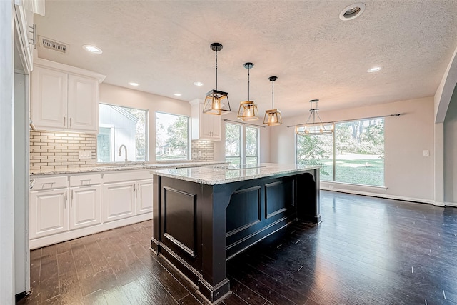 kitchen with tasteful backsplash, light stone counters, a kitchen island, sink, and white cabinetry