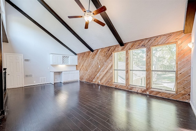 unfurnished living room with dark hardwood / wood-style flooring, lofted ceiling with beams, ceiling fan, and wooden walls