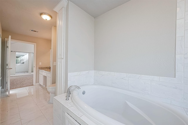 bathroom featuring tiled tub, vanity, and toilet