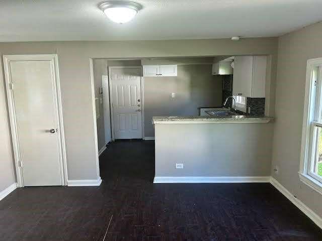 kitchen featuring dark wood-type flooring, sink, white cabinetry, light stone counters, and kitchen peninsula