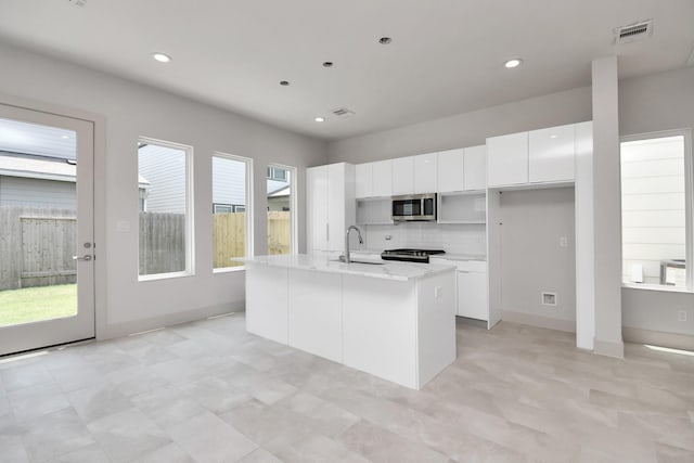 kitchen with sink, a kitchen island with sink, stainless steel appliances, white cabinets, and decorative backsplash