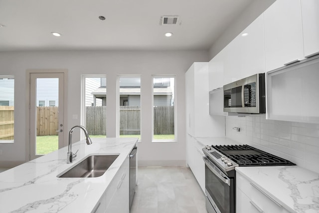 kitchen with sink, stainless steel appliances, light stone counters, decorative backsplash, and white cabinets