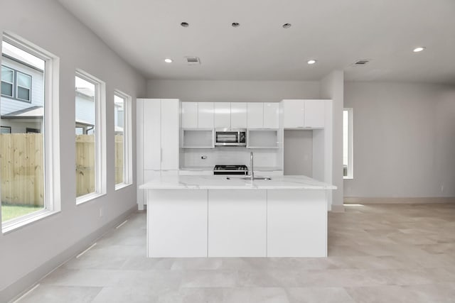 kitchen featuring a center island with sink, white cabinetry, a healthy amount of sunlight, and sink