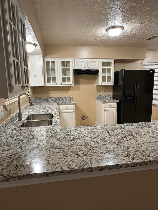 kitchen with white cabinets, black fridge, sink, a textured ceiling, and light stone counters