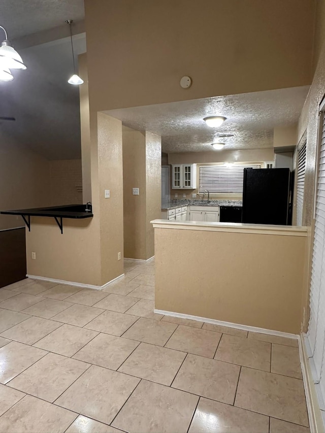 kitchen with black refrigerator, kitchen peninsula, light tile patterned floors, pendant lighting, and white cabinetry