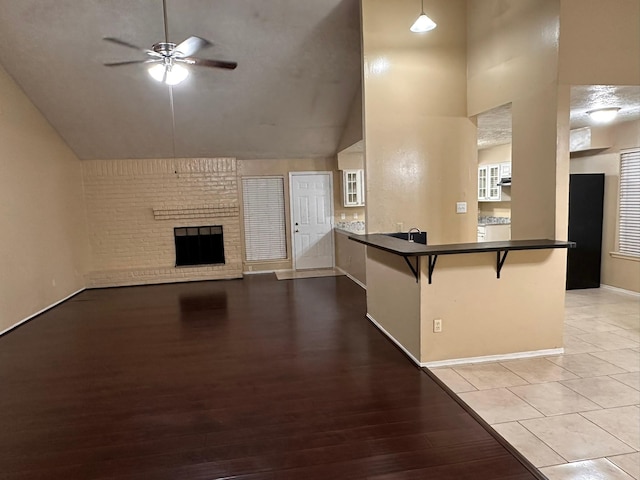 unfurnished living room featuring ceiling fan, light wood-type flooring, a fireplace, and high vaulted ceiling