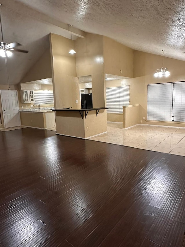 interior space with high vaulted ceiling, ceiling fan with notable chandelier, sink, light wood-type flooring, and a textured ceiling