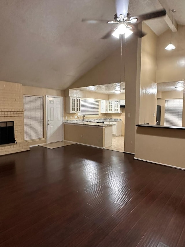 unfurnished living room with a brick fireplace, ceiling fan, sink, lofted ceiling with beams, and hardwood / wood-style flooring